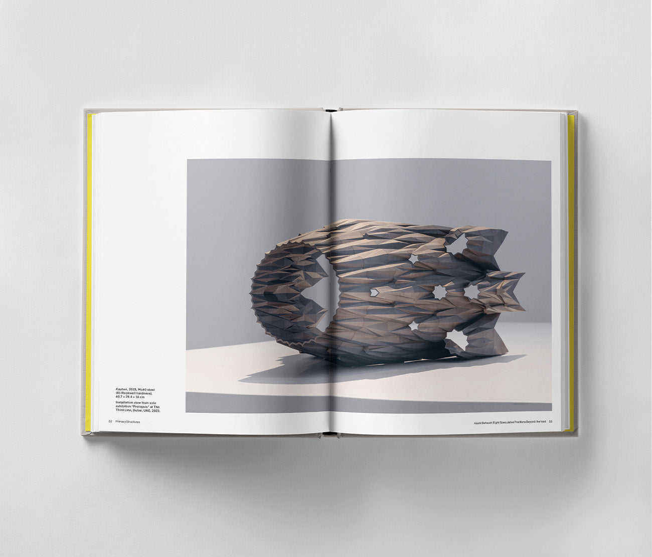 The book "Sahand Hesamiyan: Primary Structures" by Black Dog Online opens to a stunning photograph of a geometric wooden sculpture with triangular patterns on a gray backdrop, reflecting Islamic and Persian architectural influences in a modern artistic blend.