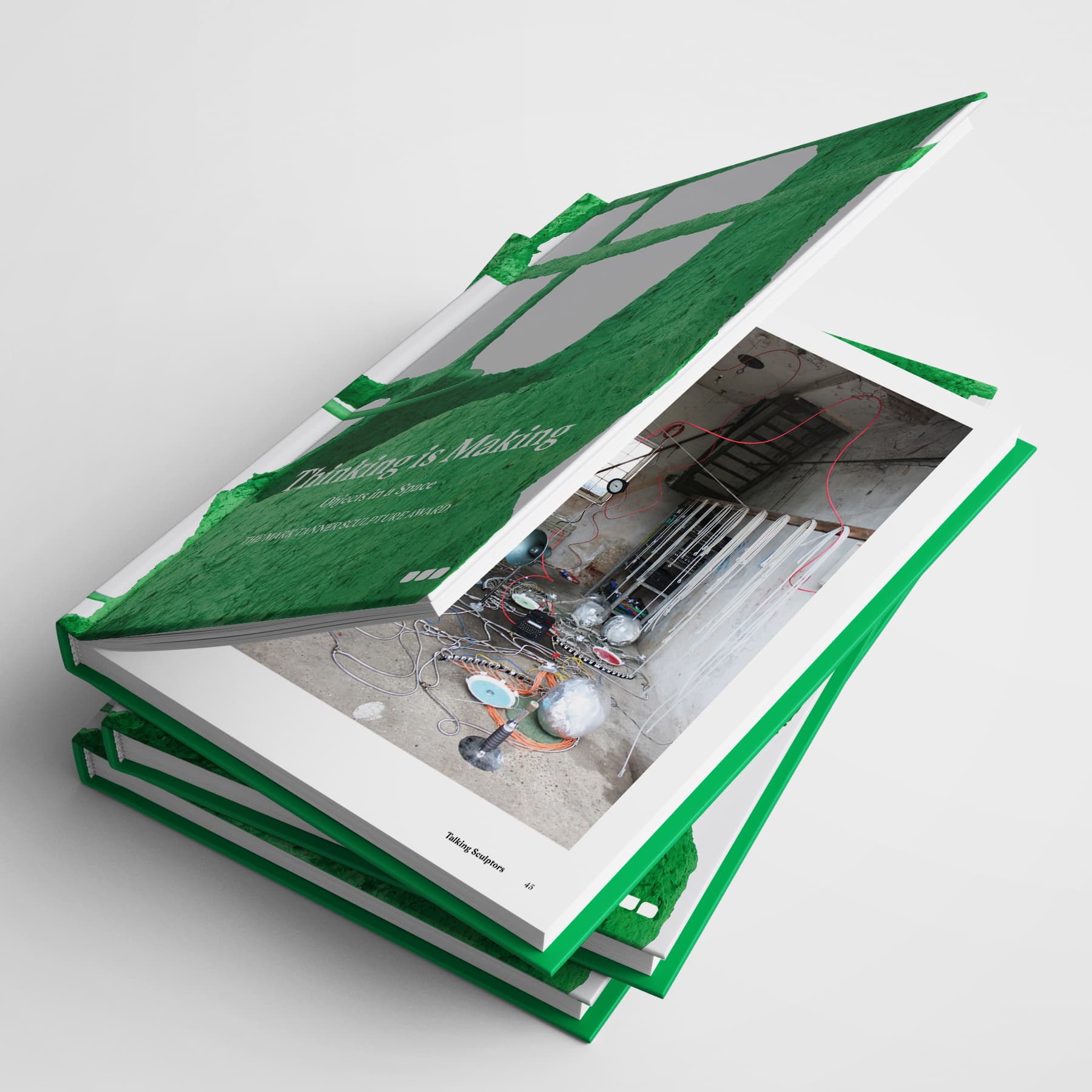 Stack of three green hardcover books with the top one open, revealing an image of a room under construction with tools and wires scattered, highlighting contemporary sculptural practice—Thinking is Making: Objects in Space The Mark Tanner Sculpture Award by Black Dog Online.