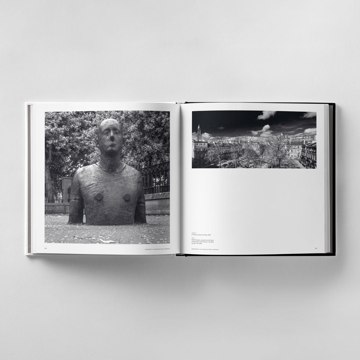 An open book from Black Dog Online's "Edinburgh: An Architectural Portrait" reveals a black and white human sculpture photo on the left and a cityscape architectural image on the right, resting on a plain, light surface reminiscent of James Reid's meticulous photography style.