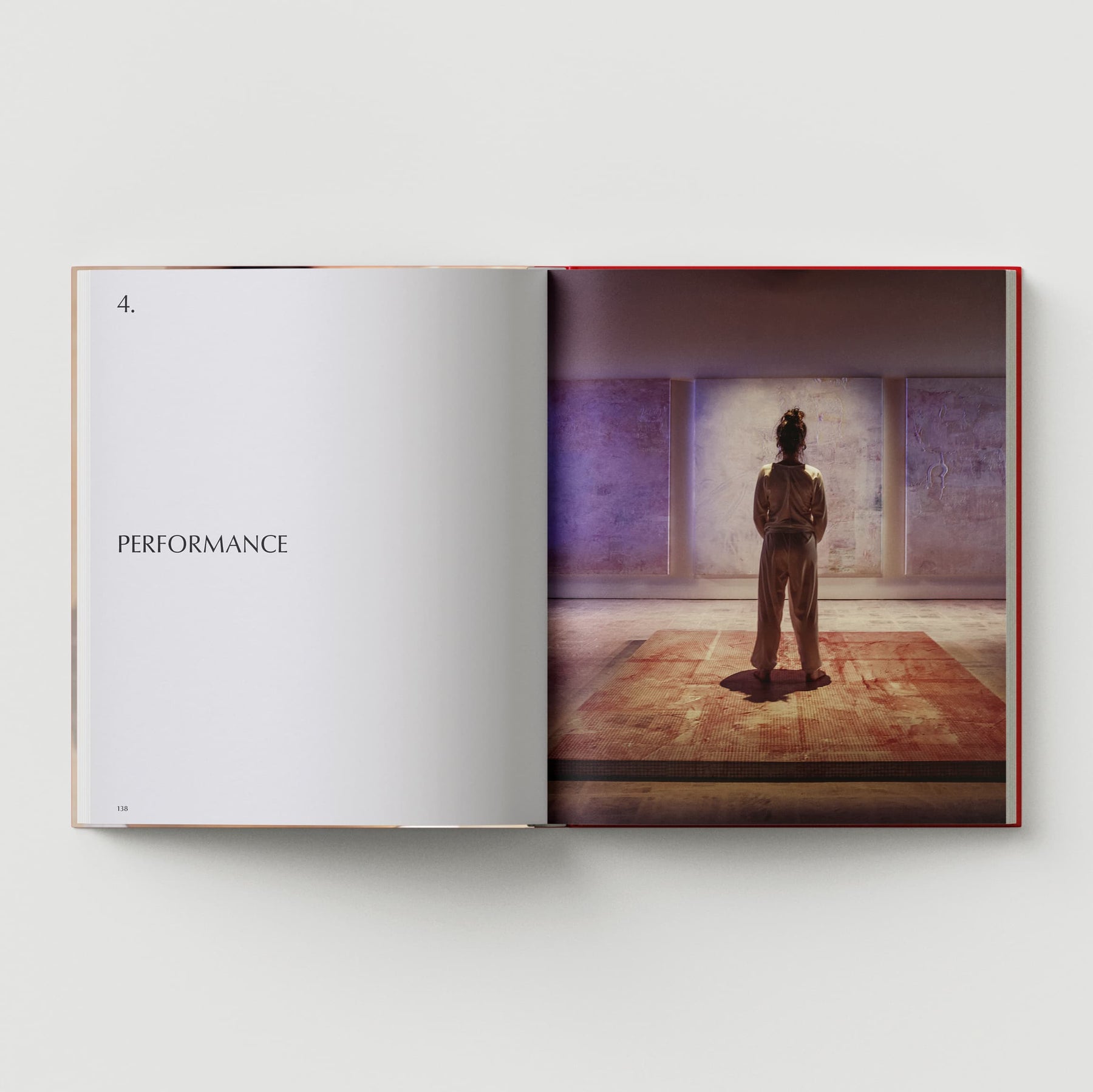 An open book displays the left page with the word "PERFORMANCE," while the right page showcases an image of Mandy El-Sayegh, a contemporary artist, standing in an art gallery, as featured in "The Makeshift Body: Mandy El-Sayegh" by Black Dog Online.