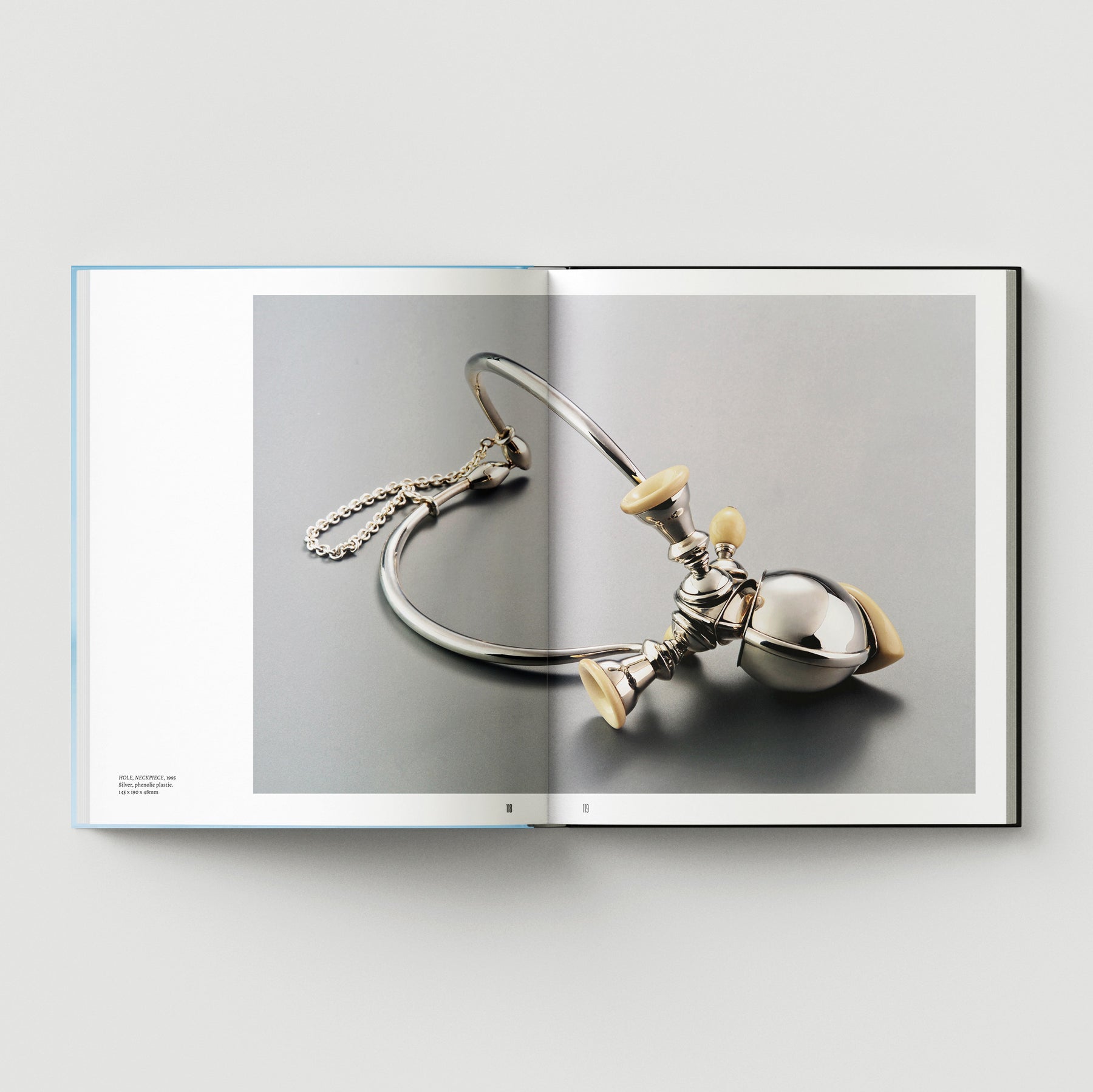 An open book shows "Formula + Fetish" by Black Dog Press, featuring British artist Mark Woods’ photo of a metallic stethoscope with cream earpieces on gray—a subtle fusion of jewellery and fine art.