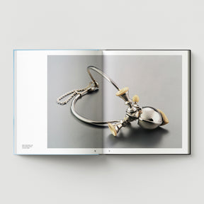 An open book shows "Formula + Fetish" by Black Dog Press, featuring British artist Mark Woods’ photo of a metallic stethoscope with cream earpieces on gray—a subtle fusion of jewellery and fine art.
