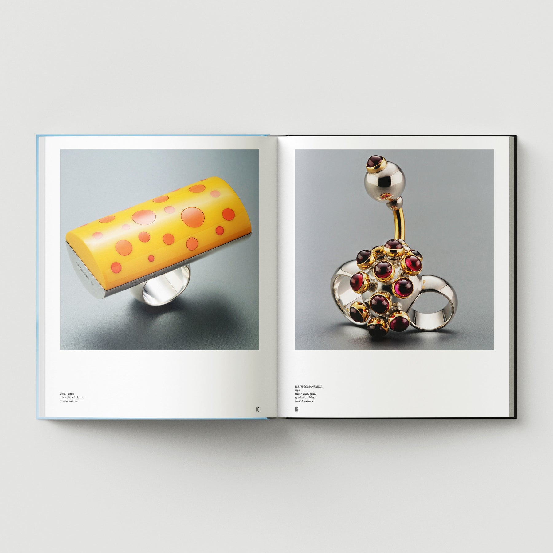 Open book from Black Dog Press’s "Formula + Fetish" shows two pages: left displays a yellow ring with orange dots, right features a silver ring with spherical and gem-like details by British artist Mark Woods.