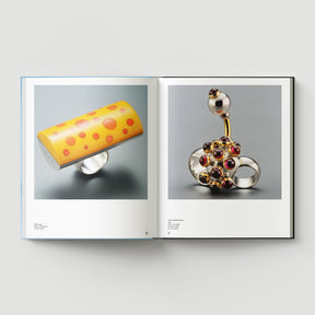 Open book from Black Dog Press’s "Formula + Fetish" shows two pages: left displays a yellow ring with orange dots, right features a silver ring with spherical and gem-like details by British artist Mark Woods.