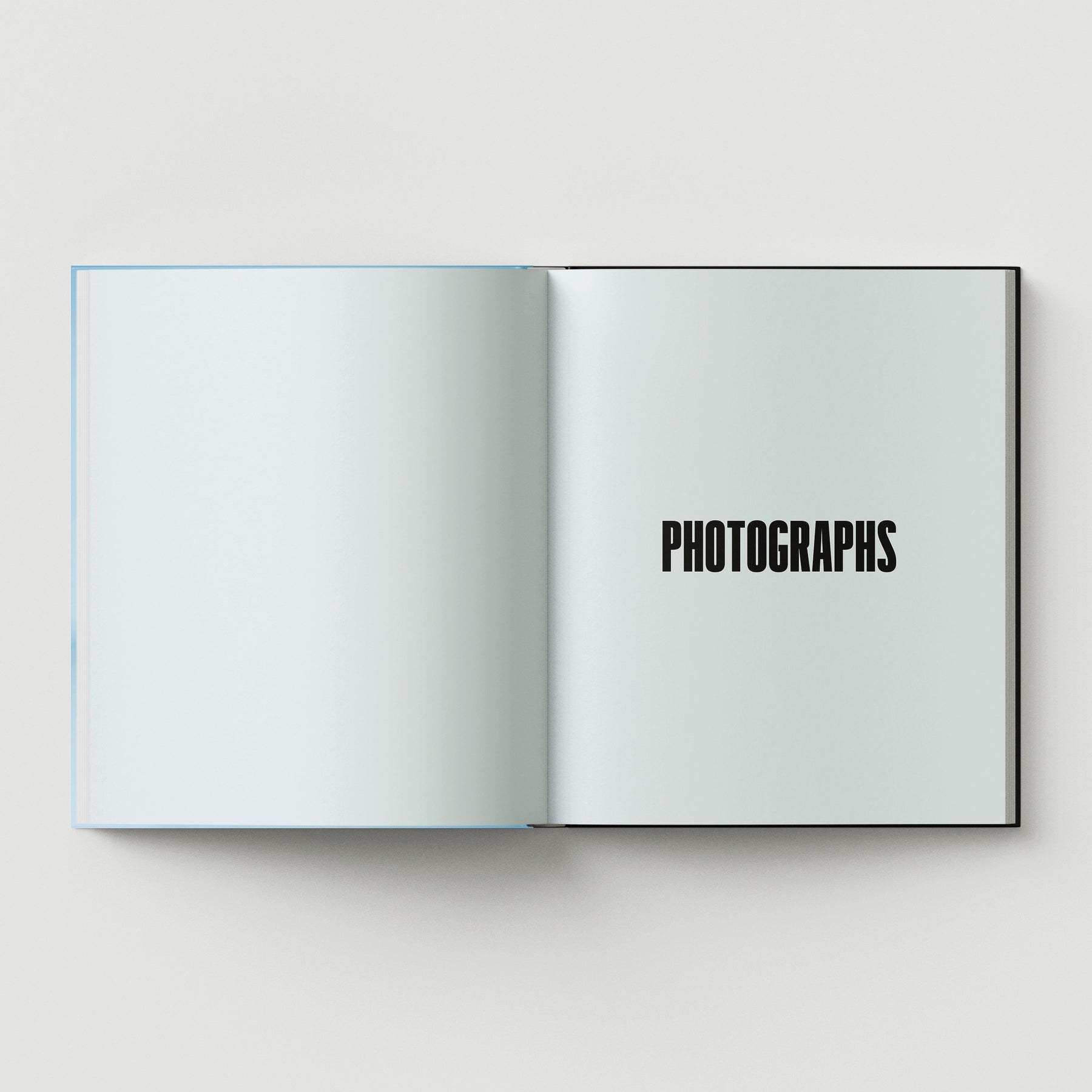 An open book from Black Dog Press titled "Formula + Fetish" displays a blank left page and a right page with "PHOTOGRAPHS" in bold, black letters—an evocative piece reminiscent of British artist Mark Woods' jewellery and fine art.