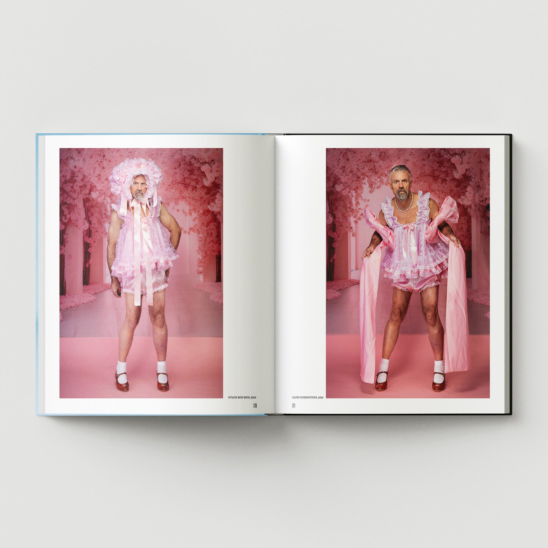 An open book from Black Dog Press’s "Formula + Fetish" shows two photos of a bearded man in a pink frilly dress, bonnet, and white socks against a pink background, reflecting Mark Woods’ fusion of jewellery and fine art.