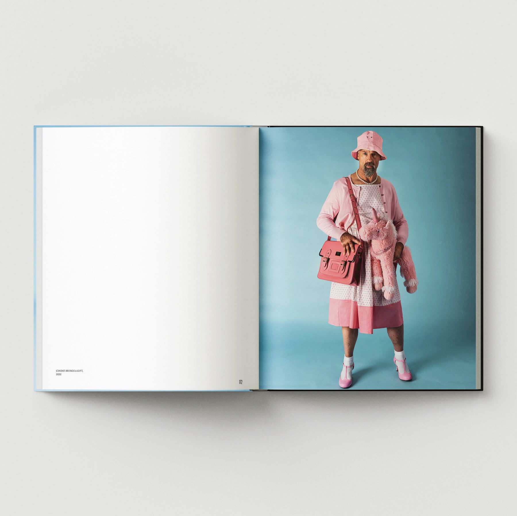 British artist Mark Woods appears in pink clothing with a pink bag and stuffed animal, set against a light blue backdrop, on the right page of "Formula + Fetish" by Black Dog Press.