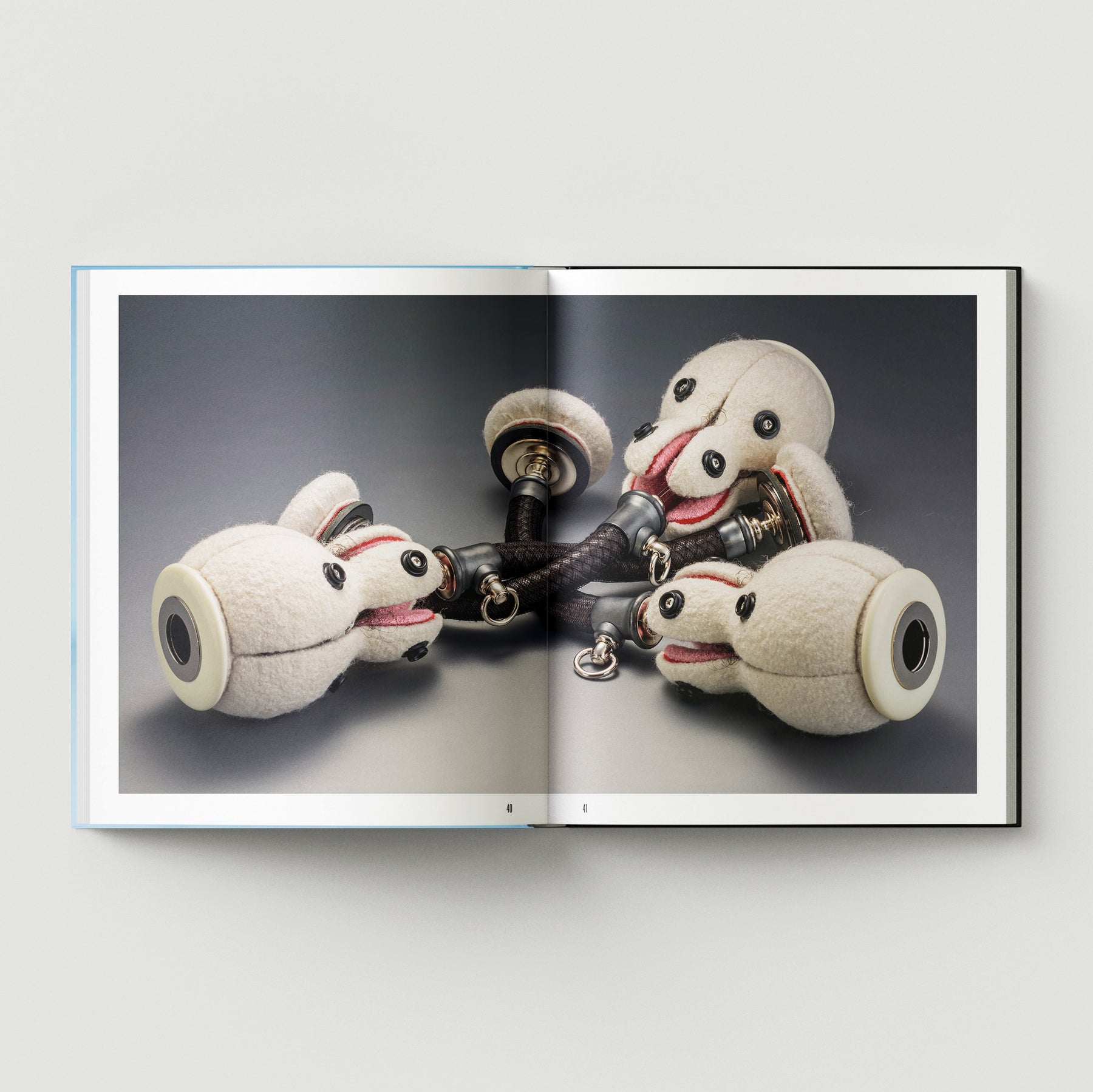 Formula + Fetish by Black Dog Press features British artist Mark Woods' photo of four plush dog heads in a circle on metal fixtures, merging jewellery and fine art against a neutral backdrop.