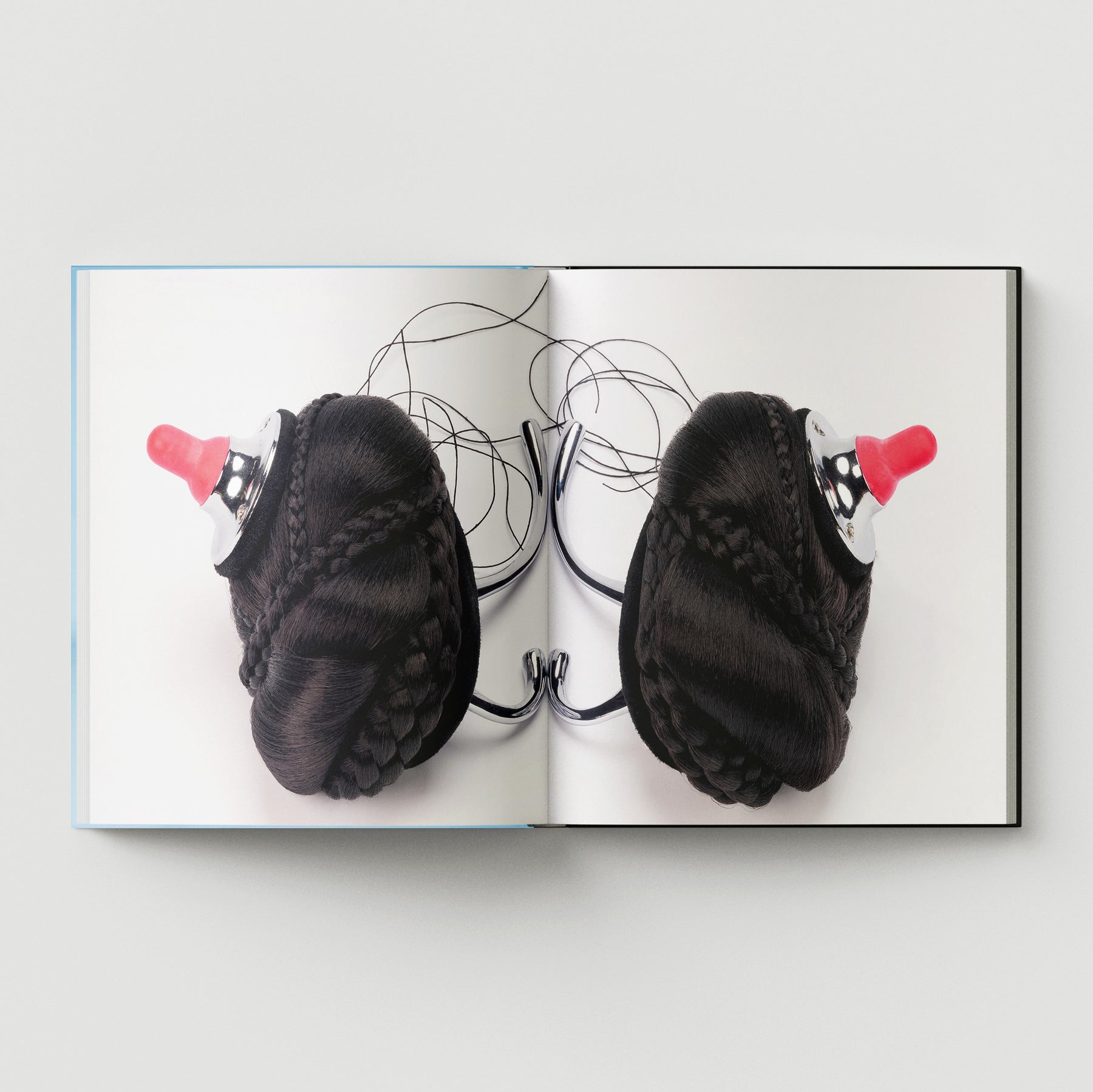 Formula + Fetish by Black Dog Press features British artist Mark Woods’s work: black braided hair buns with red baby bottle nipples atop metal hooks, blending jewellery and fine art on a white background.
