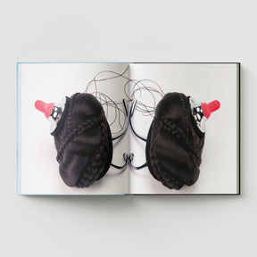 Formula + Fetish by Black Dog Press features British artist Mark Woods’s work: black braided hair buns with red baby bottle nipples atop metal hooks, blending jewellery and fine art on a white background.