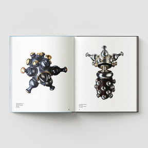 An open book titled "Formula + Fetish" by Black Dog Press shows two pages with images of metallic, abstract, symmetrical sculptures merging jewellery and fine art against a white background.